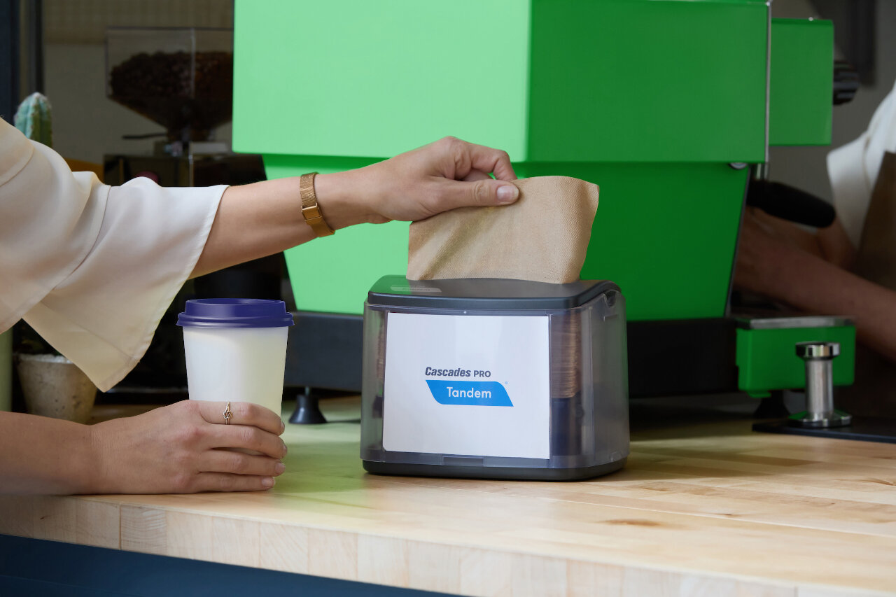 A ladies hand pulling a napkin out of Cascades Pro Napkin Dispenser